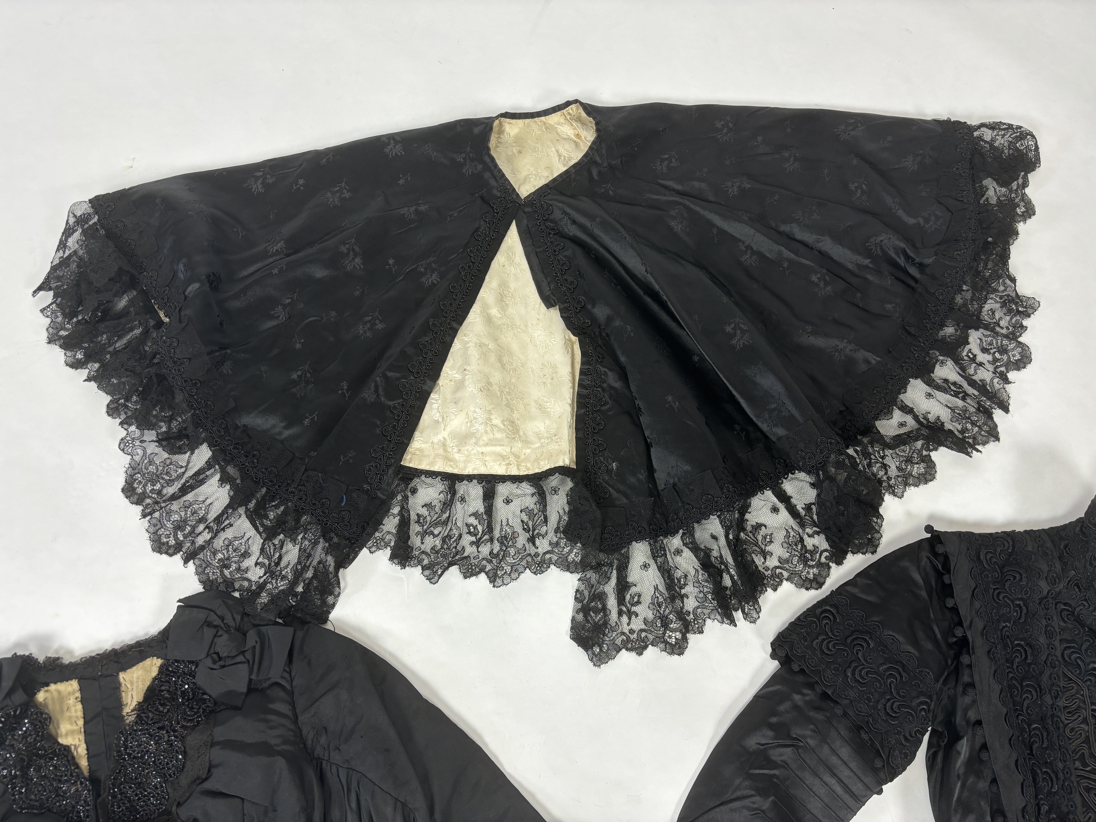 Two lady's Victorian black satin and lace, bead trimmed bodices, together with a black lace cape, a black satin cape, a small collection of coloured feathers and a child’s white worked pinafore